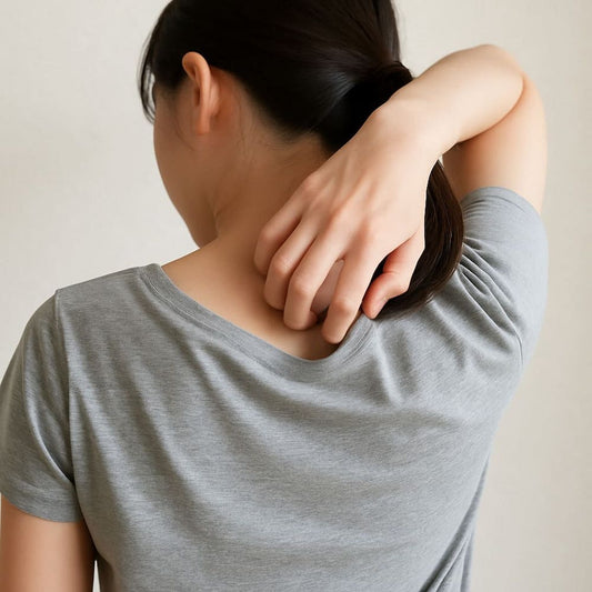背中を向けた女性が、首の下あたりを右手で掻いている写真